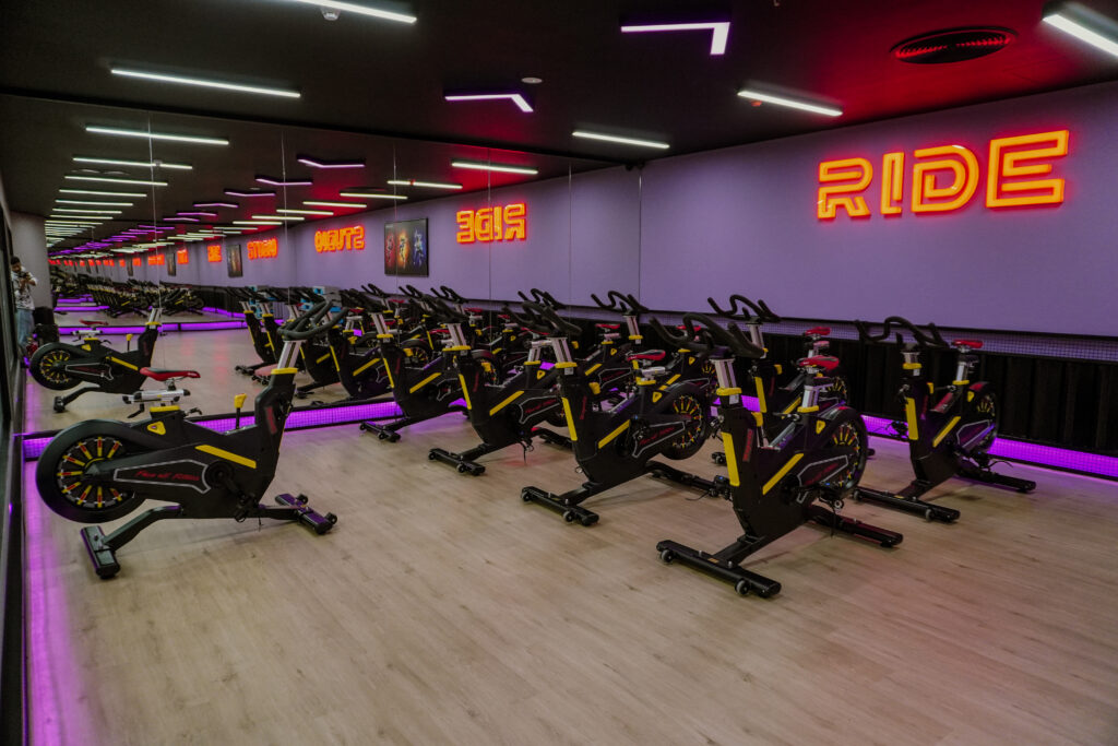 Indoor cycling class at Face Off Fitness Ride Zone with participants riding stationary bikes.